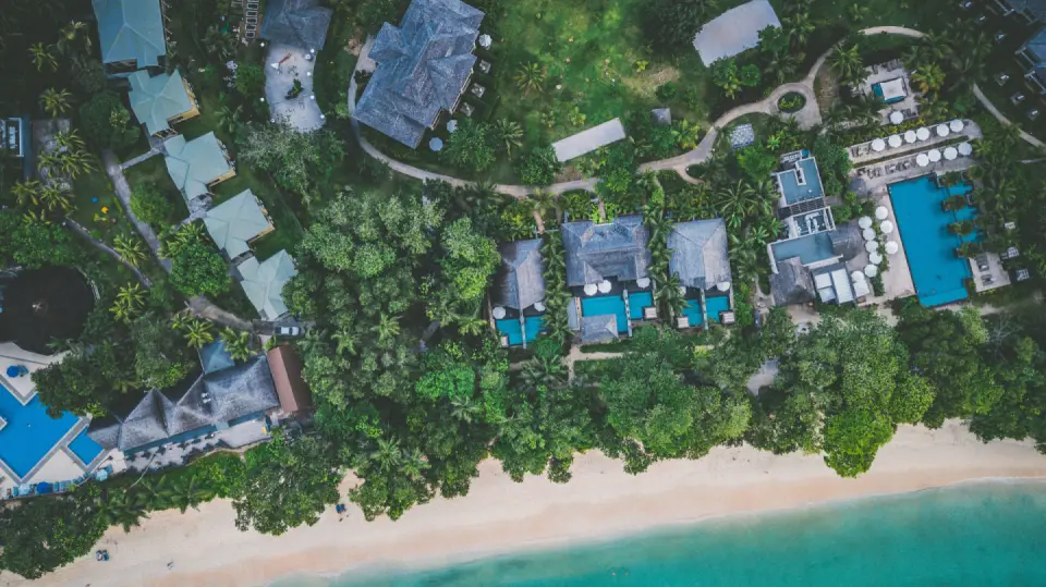 Aerial view of a tropical island resort surrounded by lush green vegetation, white sandy beaches, and turquoise ocean water in Seychelles.